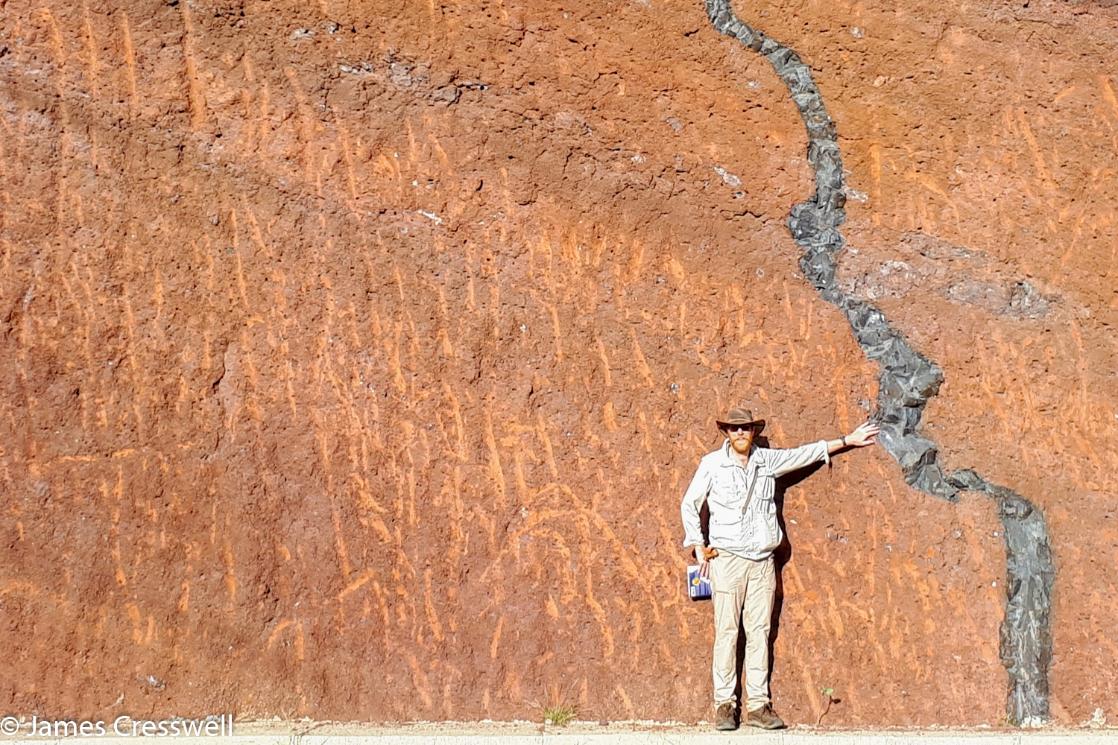 A photograph of James Cresswell, of GeoWorld Travel, pointing to a dyke that cuts through compacted backed scoria on La Gomera