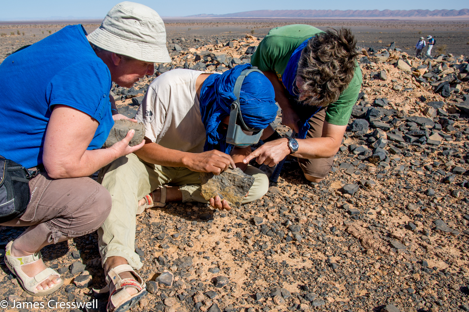 A photograph of three people examining fossils in the Moroccan desert, taken on a GeoWorld Travel geology tour, holiday and trip 