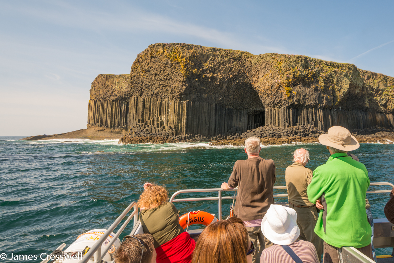 An image of people in the foreground on a boat looking at Fingals Cave in Scotland, taken on a GeoWorld Travel geology tour, holiday and trip