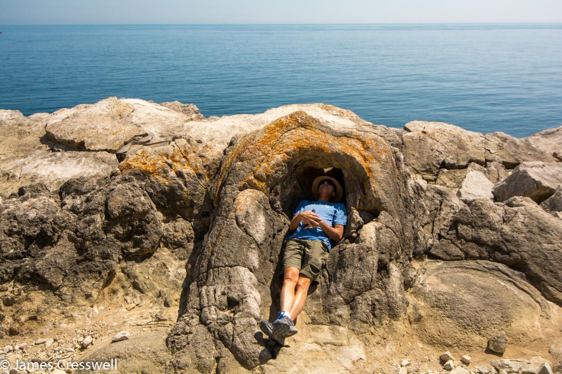 A photograph of a man lying inside a fossilised tree at Lulworth Cove, taken on the GeoWorld Travel England and Wales geology trip, tour and holiday