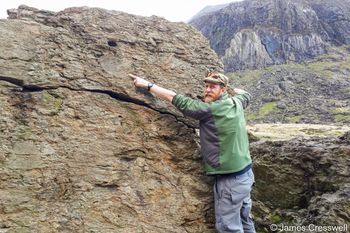 A photograph of James Cresswell pointing to an Ordovician volcanic bomb in the Cromlech Boulders, taken on a GeoWorld Travel geology trip, tour and holiday of Wales