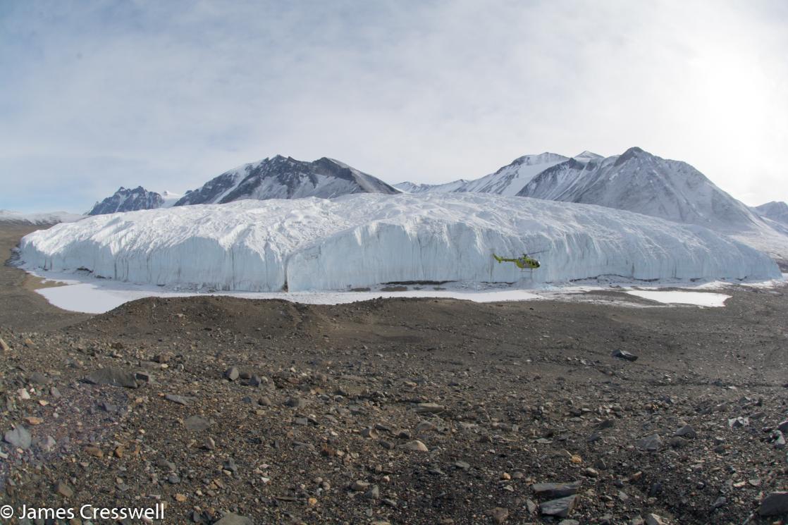 Photograph of a helicopter flying in front a piedmont glacier, the Canada Glacier, in Antarctica's Dry Valleys on a PolarWorld Travel placed cruise