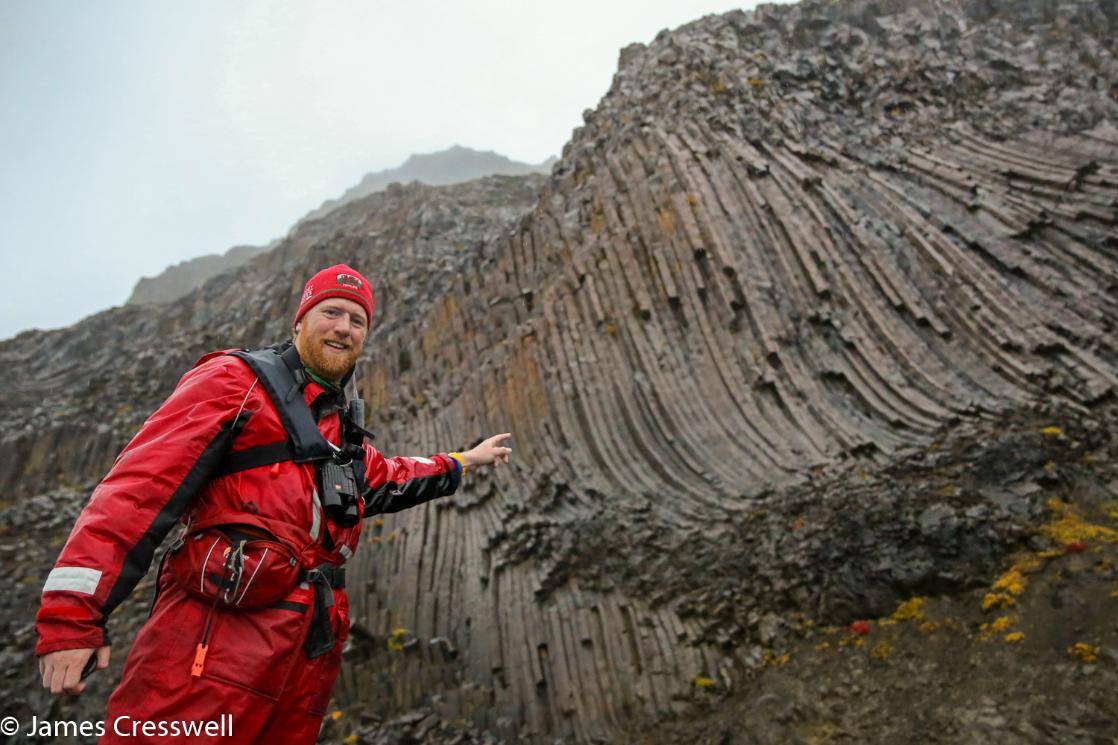 A photograph of James Cresswell pointing to columnar basalt in East Greenland