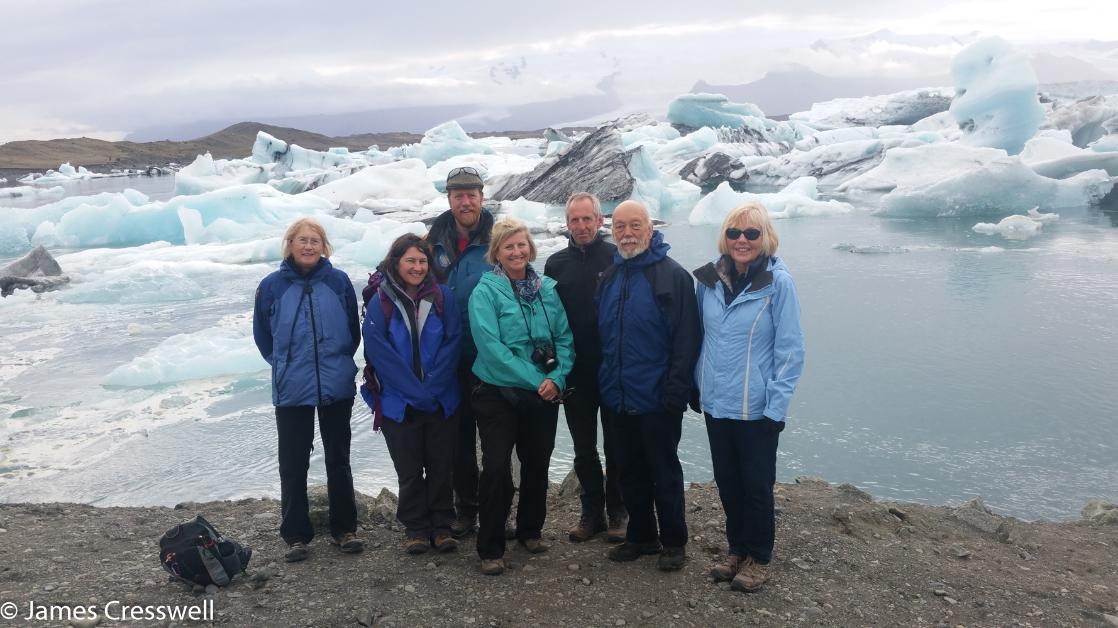 A photograph of a group of seven people standing in front of a lagoon full of icebergs, the Jokulsarlon lagoon, taken on a GeoWorld Travel geology trip and scenic holiday