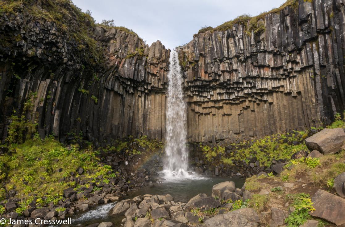 A photograph of waterfall pouring over a cliff of columnar basalt, Svartifoss waterfall, taken on the GeoWorld Travel geology trip and volcano holiday