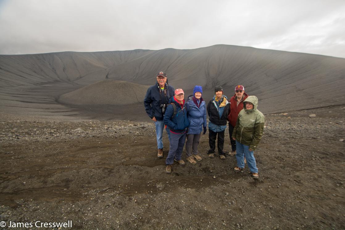A photograph of six people standing on the rim of a volcanic tuff cone, the Hverfjall tephra cone, taken on a GeoWorld Travel geology trip and volcano holiday