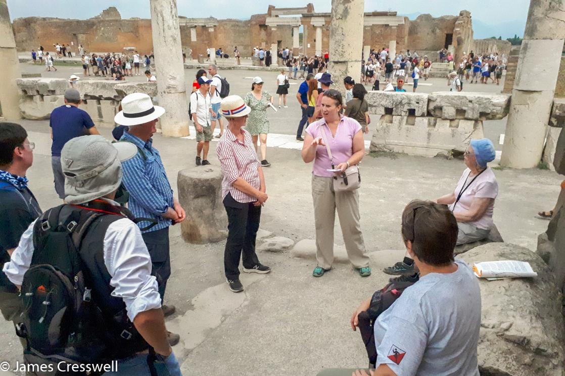 A photograph of archaeologist Abby Cresswell explaining the archaeology at Pompeii, on a GeoWorld Travel Italy volcano tour and geology trip