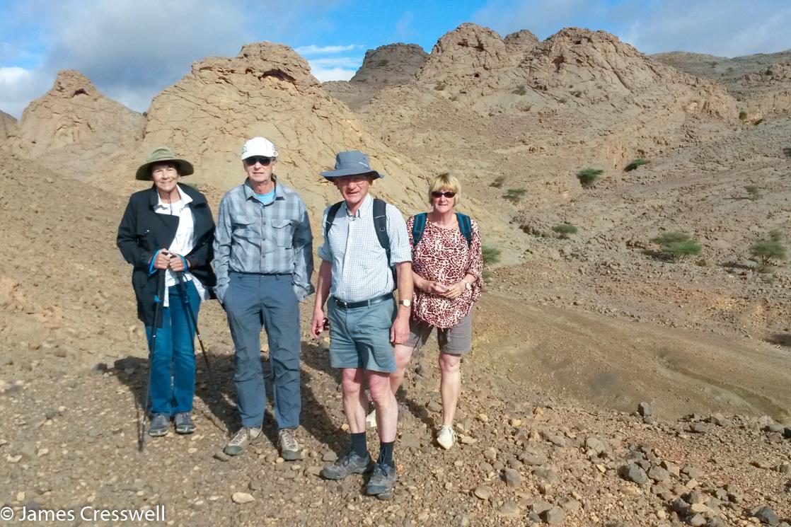 A photograph of four people standing in front of fossilised cold seep mud volcano mounds, the Kess Kess or Hamar Laghdad mounds, taken on a GeoWorld Travel fossil and geology trip, tour and holiday