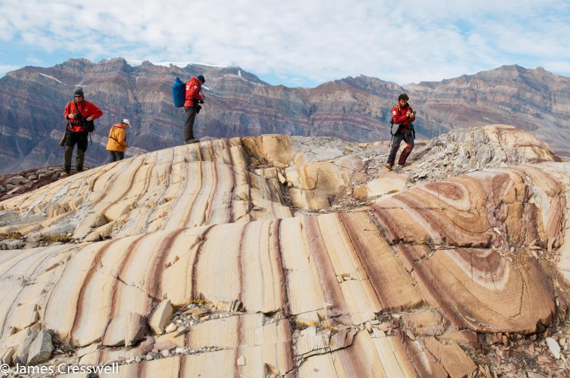 A photograph of four people standing on colourful rocks at Segelsallskarpet in North East Greeenland National Park, taken on a GeoWorld Travel geology trip, tour and holiday