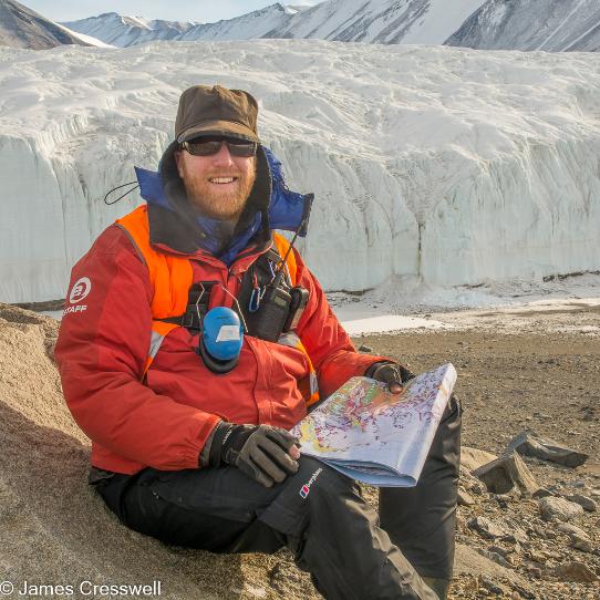 A photograph of James Cresswell reading a geological map in the McMurdo Dry Valleys of the Ross Sea area of Antarctica.