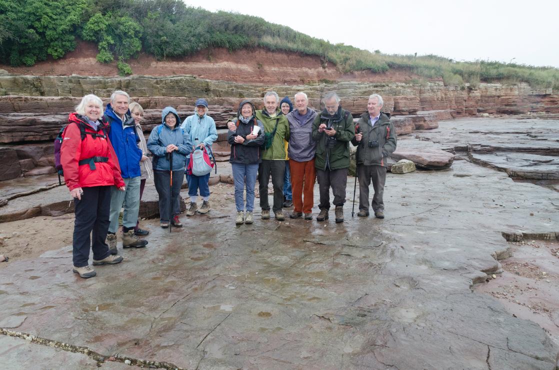 A  photo of a GeoWorld Travel U3A group with dinosaur tracks, Wales 