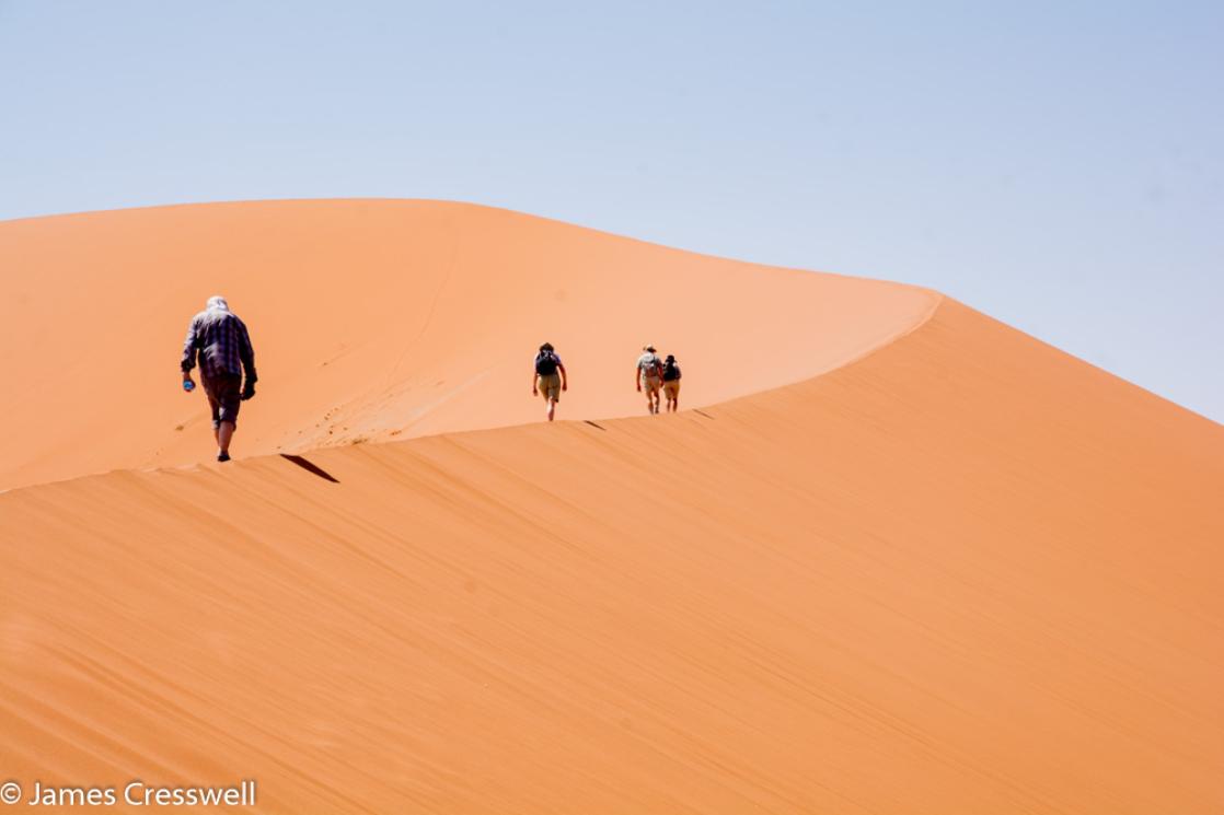 A photograph of four people climbing a sand dune in the Namib Desert, taken of a GeoWorld Travel Namibia Geology trip, tour and holiday