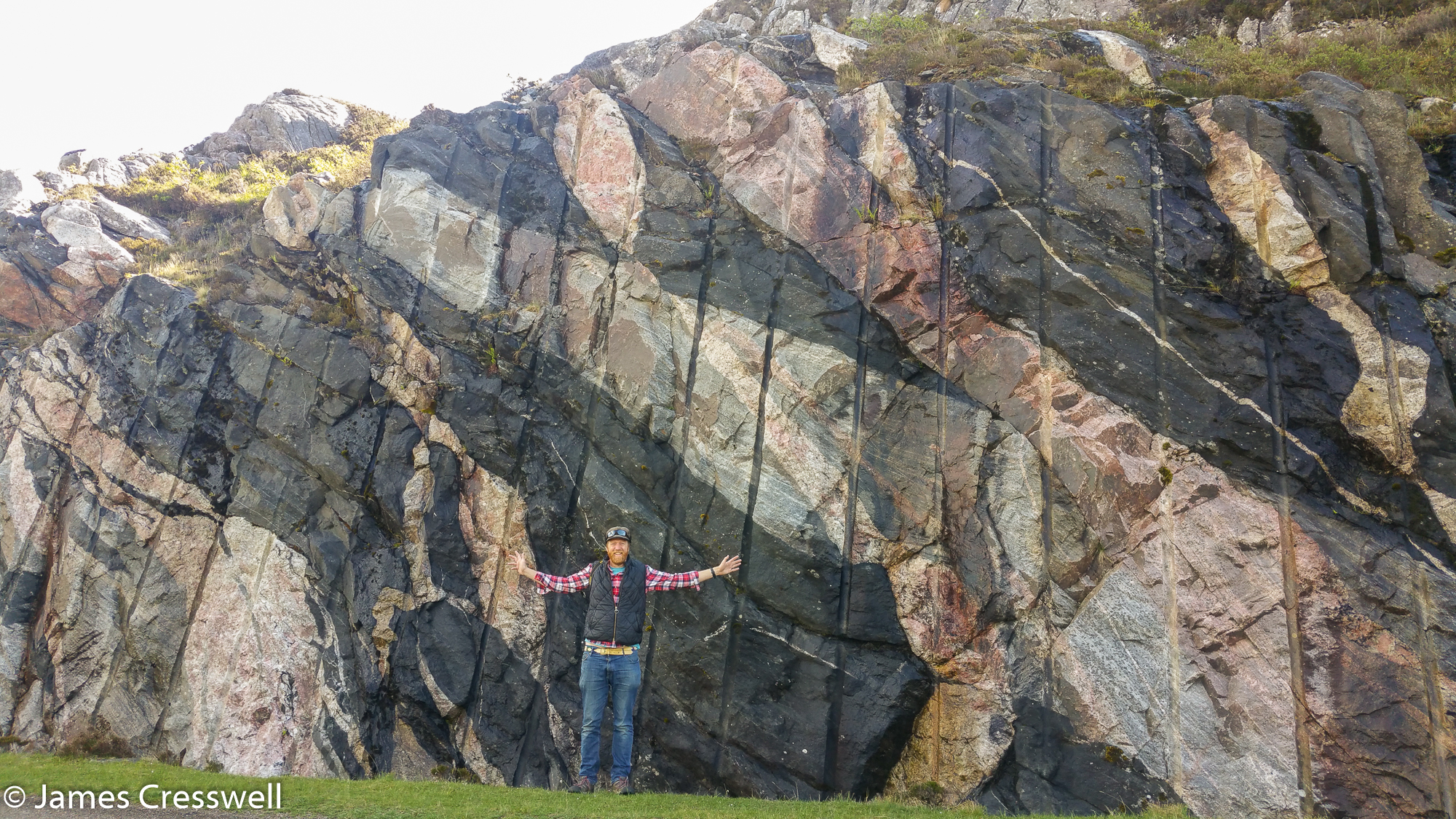 A photograph of James Cresswell in front of multi-coloured rock, the Multi-coloured rock stop in the North West Highlands Geopark, taken on a GeoWorld Travel Scotland geology trip, tour and holiday