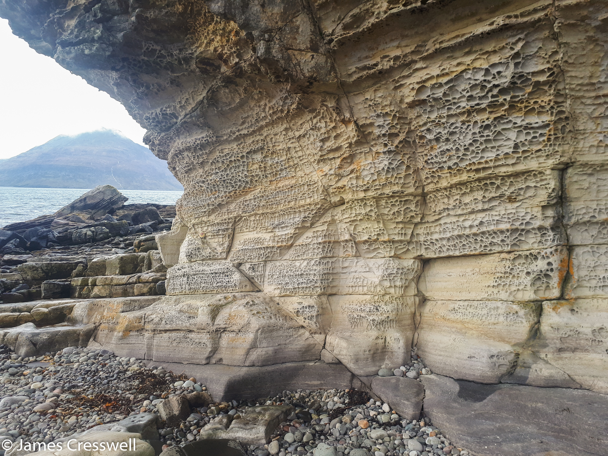 A photograph of a small yellow cliff covered in Honeycomb weathering at Elgol, Isle of Skye, taken on a GeoWorld Travel Scotland geology trip, tour and holiday