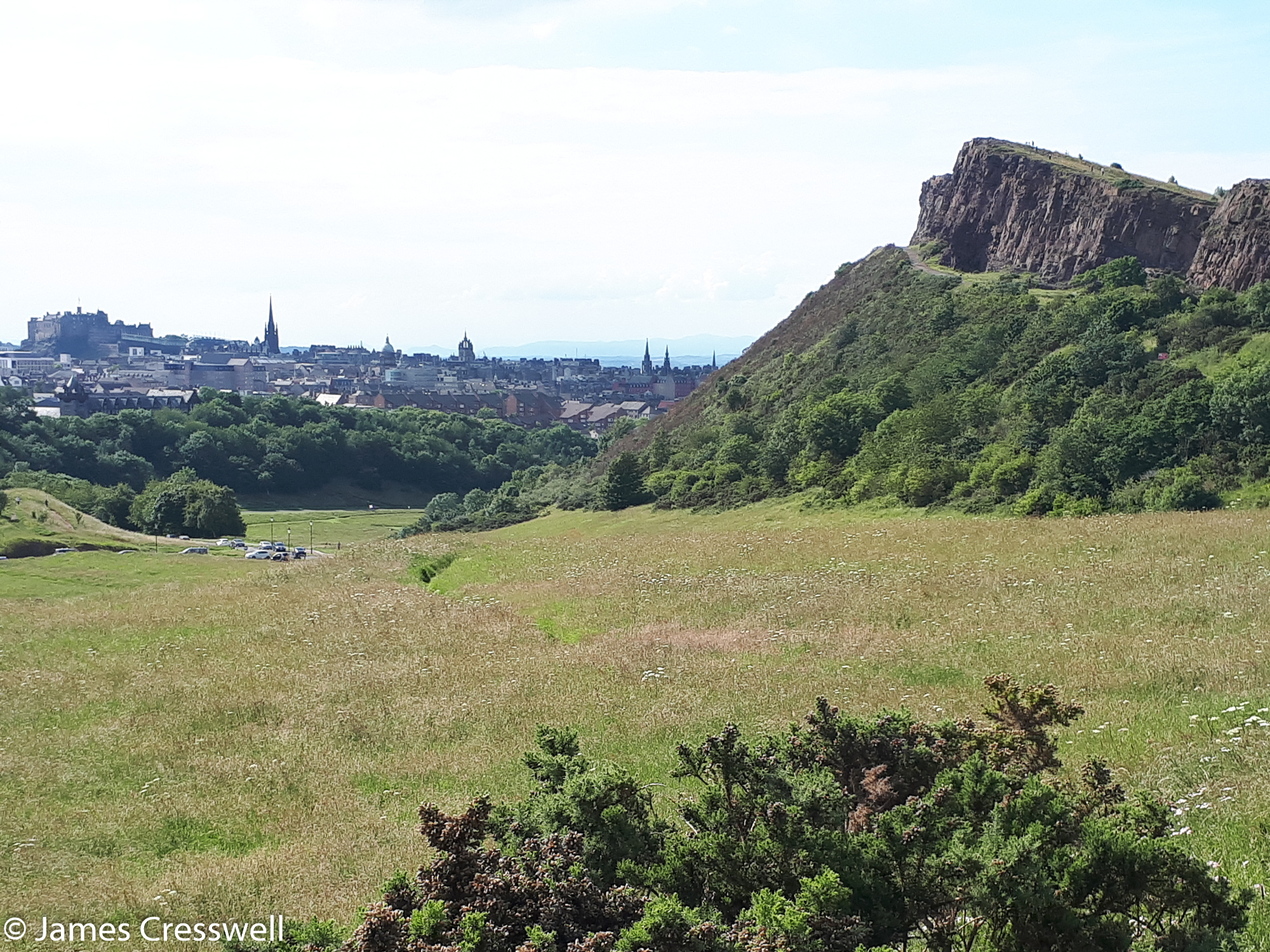 A photograph of small rock cliffs, Salisbury Crags, with the city of Edinburgh in the background, Holyrood Park, taken on a GeoWorld Travel Scotland geology trip, tour and holiday Edinburgh