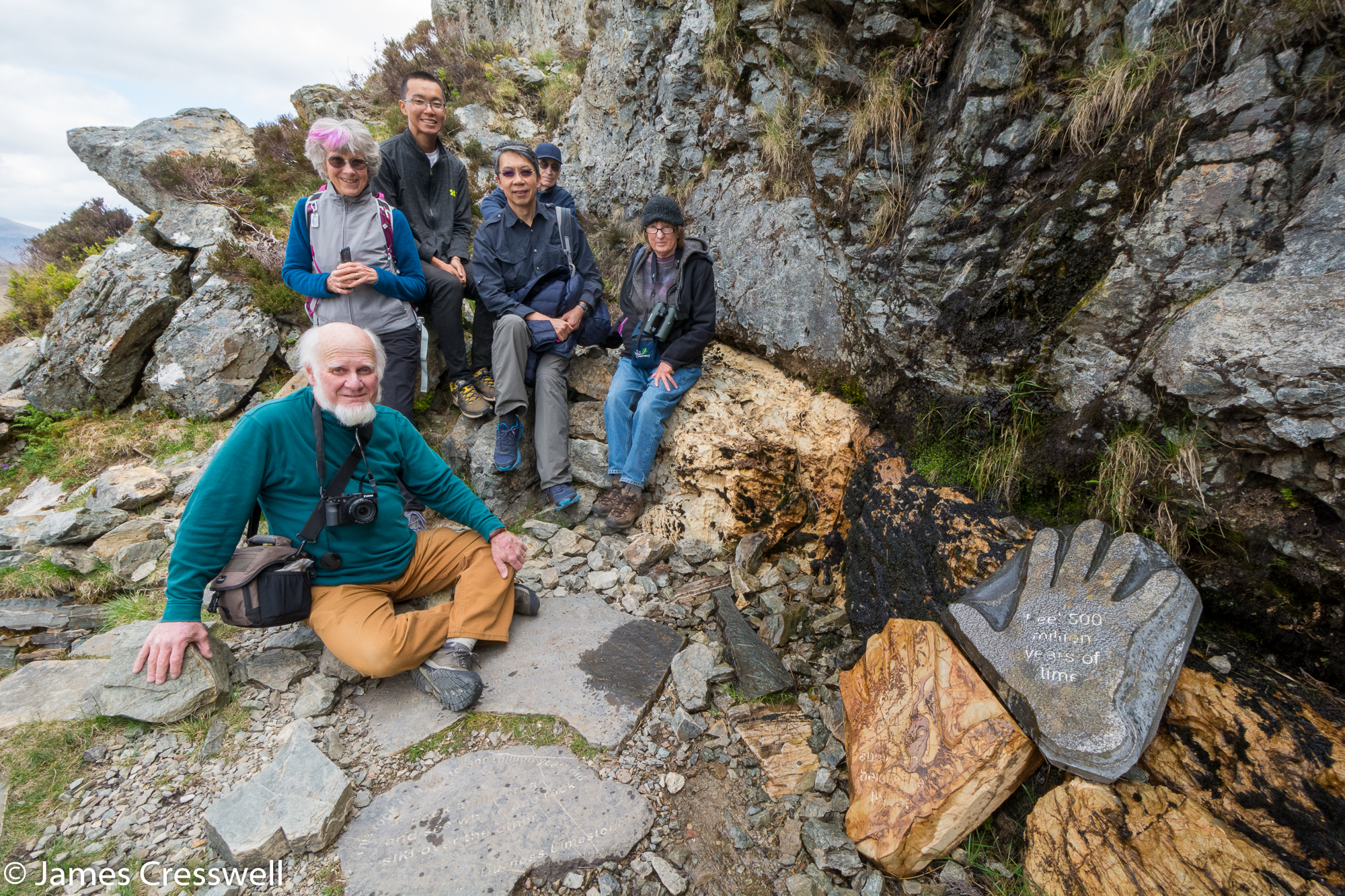 A photograph of six people sitting on the Moine Thrust at Knockan Crag, taken on a GeoWorld Travel Scotland geology trip, tour and holiday