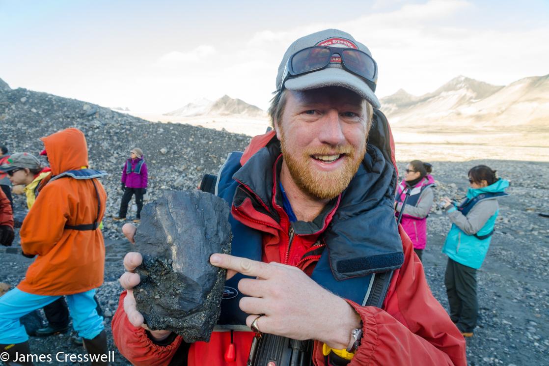 A photograph of James Cresswell Director of GeoWorld Travel & PolarWorld Travel with pointing to a tree fossil in Trygghamna, Spitsbergen,Svalbard
