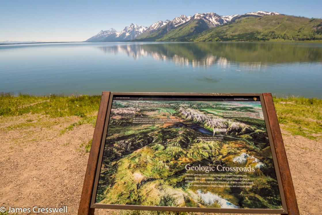 A photograph of a sign board and the Grand Teton Mountains, taken on a GeoWorld Travel USA geology trip, tour and holiday