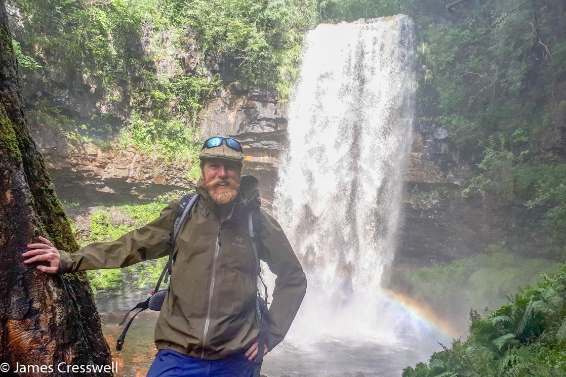 A photograph of James Cresswell standing in front of Sgwd Henrhyd on a GeoWorld Travel waterfall tour, trip and holiday